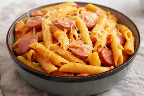 Penne z sosem pomidorowym i plasterkami kiełbasy, posypane parmezanem. Pyszny makaron z kiełbasą w misce.