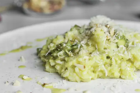 Kremowe risotto ze szparagami, posypane parmezanem i migdałami, na białym talerzu.