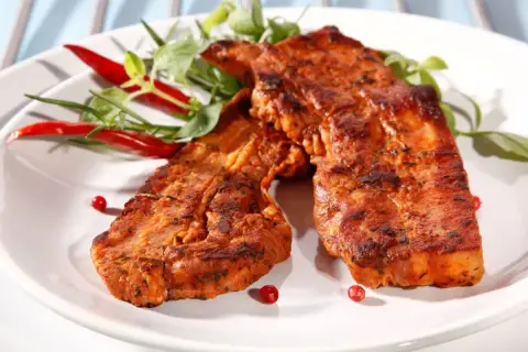Dwa soczyste kawałki boczku w aromatycznej marynacie, podane z papryczkami chili i zielonymi ziołami.
