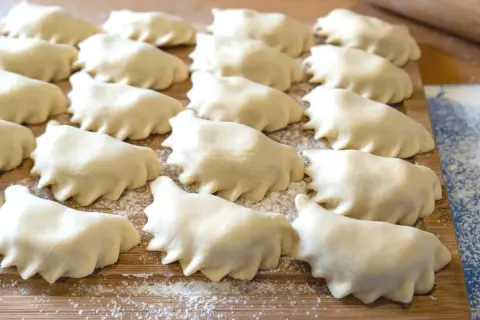 Rządki surowego ciasta na pierogi ułożone na desce, posypanej mąką.