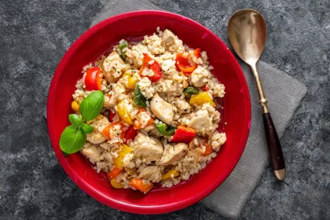 Pyszne risotto z kurczakiem, kolorową papryką i świeżą bazylią, podane w czerwonej misce.