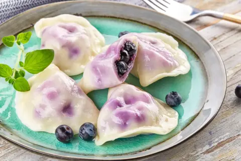 Pyszne pierogi z jagodami na turkusowym talerzu, ozdobione świeżymi borówkami i gałązką ziół.