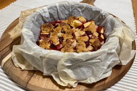 Pyszne owoce pod kruszonką, zapieczone w papierze do pieczenia, czekają na talerzu.
