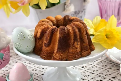 Wilgotna babka wielkanocna dwukolorowa, ozdobiona wielkanocnymi pisankami i żółtymi żonkilami, zapowiada wiosenne święta.