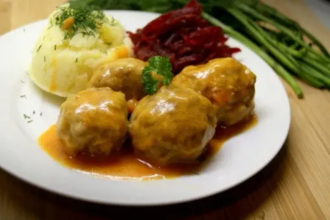 Pyszne klopsiki w sosie pomidorowym, podane z purée ziemniaczanym i buraczkami. Danie ozdobione natką pietruszki i koperkiem.