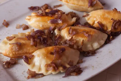Pyszne pierogi z mięsem, posypane chrupiącą cebulką, kuszą swoim wyglądem.