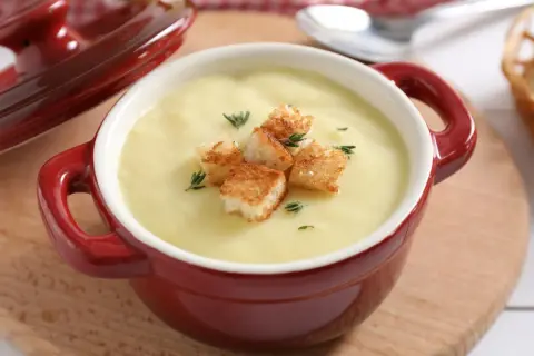 Aksamitna zupa cebulowa krem, udekorowana chrupiącymi grzankami i gałązkami tymianku, podana w czerwonej kokilce.