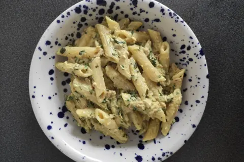 Penne z kremowym sosem, tuńczykiem i natką pietruszki w talerzu w granatowe cętki. Pyszny makaron z tuńczykiem.