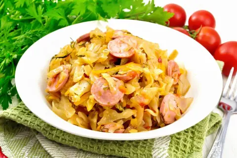 Pyszny bigos z młodej kapusty z kiełbasą, podany na białym talerzu, ozdobiony zieloną natką i pomidorkami.