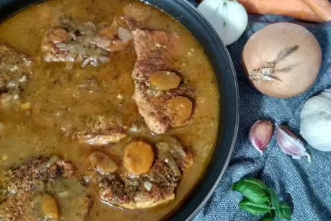 Pyszny strogonow ze schabu w sosie z cebulą i marchewką, gotowy do podania. Obok składniki: marchew, cebula, czosnek i bazylia.