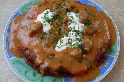 Pyszny placek po węgiersku z gulaszem, śmietaną i koperkiem na talerzu.