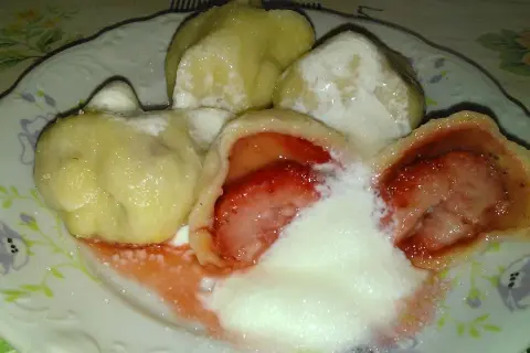 Pyszne pierogi z truskawkami, polane śmietaną i posypane cukrem, kuszą swoim wyglądem i zapachem.