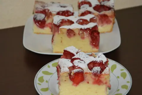 Pyszne ciasto ucierane z truskawkami, posypane cukrem pudrem, prezentuje się apetycznie na talerzykach.