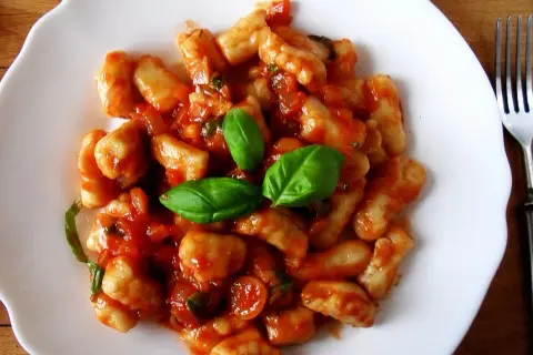 Pyszne gnocchi w sosie pomidorowym, udekorowane listkami bazylii. Idealne danie na szybki obiad.