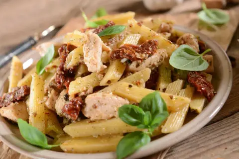 Penne z kurczakiem i suszonymi pomidorami, udekorowane świeżą bazylią. Pyszne danie, które zachwyci każdego smakosza.