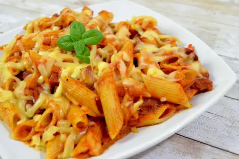 Penne z sosem pomidorowym i kawałkami pikantnego chorizo, zapieczone pod ciągnącym się serem. Udekorowane listkiem bazylii.
