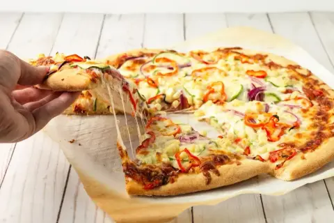 Ciepły, ciągnący się ser na kawałku pizzy z warzywami. Idealny spód do pizzy zachęca do sięgnięcia po kolejny kawałek.