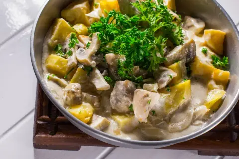Pyszna potrawka z kurczaka z ziemniakami i pieczarkami w kremowym sosie, udekorowana natką pietruszki.