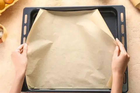 Dłonie układają papier do pieczenia na blasze. To świetne rozwiązanie, co zamiast papieru do pieczenia, gdy chcesz uniknąć przypalenia.