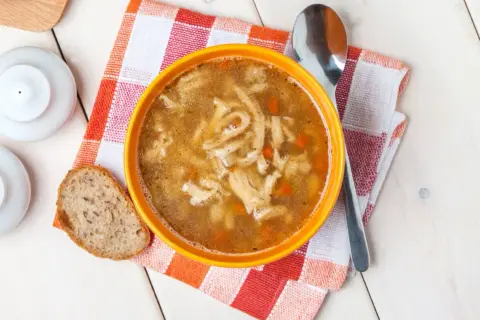 Pyszne flaki Ani gotuje, podane w pomarańczowej misce z chlebem i łyżką.