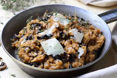 Aksamitne risotto z grzybami, udekorowane płatkami parmezanu i gałązkami tymianku, podane w metalowej patelni.