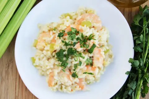 Pyszne risotto z krewetkami, ozdobione natką pietruszki, obok łodygi selera i butelka oliwy.