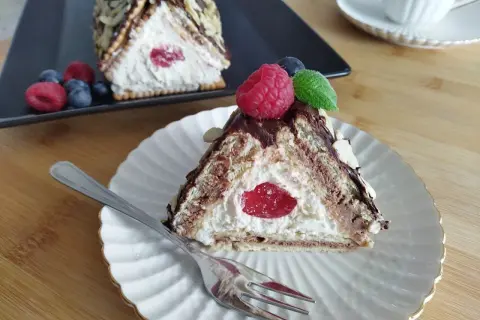 Trójkątny deser z kremem, wiśnią i malinami, przypominający chatkę Baby Jagi.