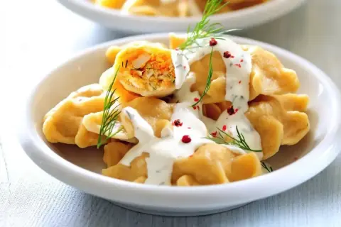 Elegancki obiad dla gości: pyszne pierogi z farszem, polane sosem śmietanowym, ozdobione koperkiem i różowym pieprzem.