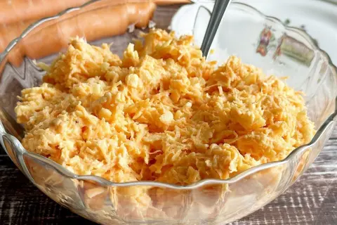 Pyszna surówka z marchewki w szklanej misie, gotowa do podania. Obok leżą świeże marchewki.
