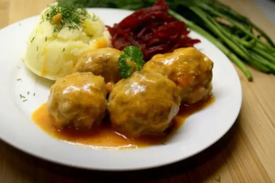 Pyszne klopsiki w sosie pomidorowym, podane z purée ziemniaczanym i buraczkami. Danie ozdobione natką pietruszki i koperkiem.