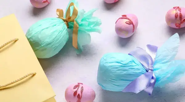 Kolorowe jajka wielkanocne, niektóre ozdobione, inne zapakowane w papier. Idealne na prezent, jakby były zrobione z naturalne barwniki do jajek.