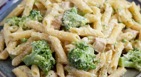 Penne z kurczakiem i kremowym sosem, obficie posypane zielonymi różyczkami brokułów. Pyszne makaron z brokułami na talerzu.