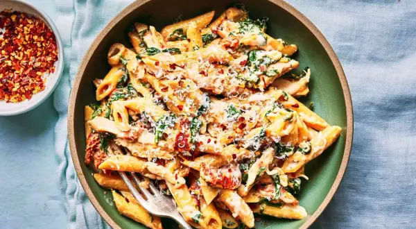 Penne w kremowym sosie ze szpinakiem i suszonymi pomidorami, posypane parmezanem i płatkami chili.