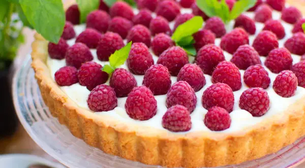 Pyszna tarta z malinami, udekorowana listkami mięty, kusi apetycznym wyglądem.