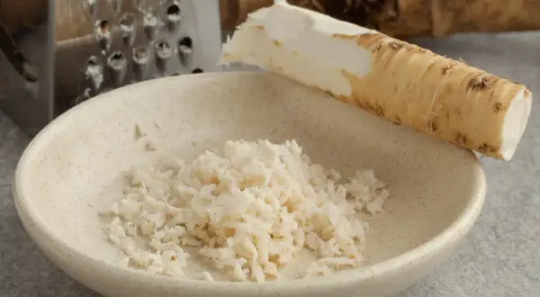 Start your culinary adventure: jak zrobić chrzan. Świeży korzeń chrzanu, tarka i miseczka z tartym chrzanem.