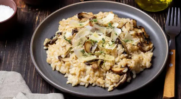 Aksamitne risotto z pieczarkami, posypane parmezanem i świeżym tymiankiem, prezentuje się apetycznie na ciemnym talerzu.