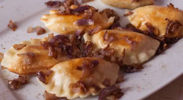 Pyszne pierogi z mięsem, posypane chrupiącą cebulką, kuszą swoim wyglądem.