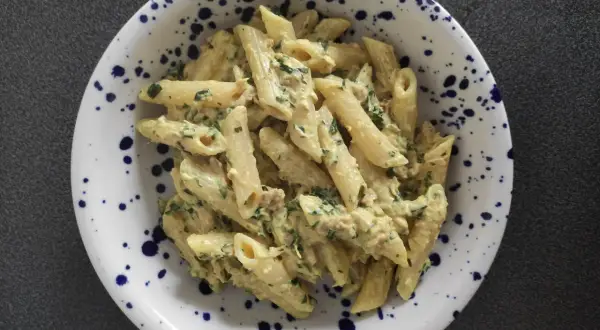 Penne z kremowym sosem, tuńczykiem i natką pietruszki w talerzu w granatowe cętki. Pyszny makaron z tuńczykiem.