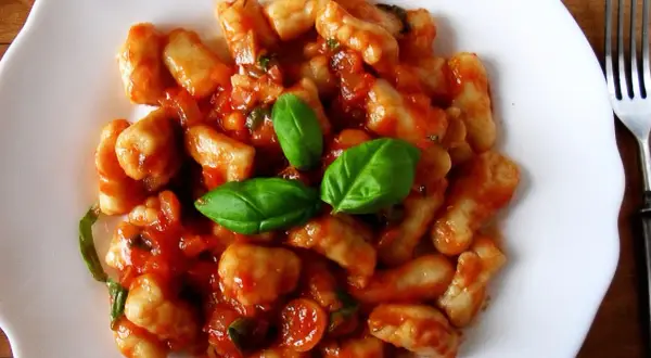 Pyszne gnocchi w sosie pomidorowym, udekorowane listkami bazylii. Idealne danie na szybki obiad.