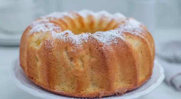 Puszysta babka na oleju, oprószona cukrem pudrem, prezentuje się apetycznie na białej paterze. Idealna na niedzielne popołudnie.