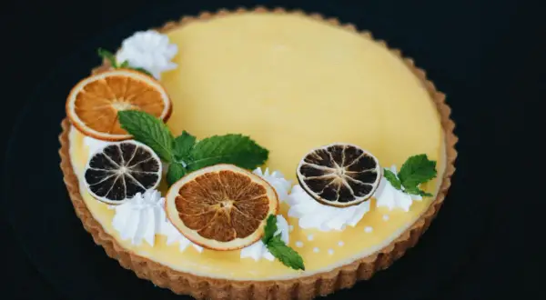 Pyszna tarta z owocami: cytrynowy krem, suszone pomarańcze i limonki, listki mięty i ozdobne kleksy bitej śmietany.
