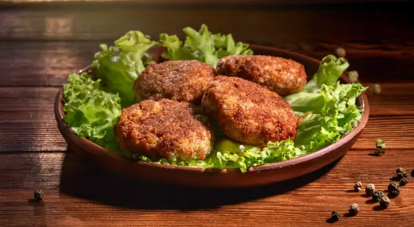 Cztery soczyste mielone z air fryer, podane na liściach sałaty, kuszą apetycznym wyglądem.