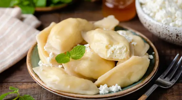 Pyszne pierogi z serem na słodko, posypane twarogiem i udekorowane miętą. Idealne na deser.