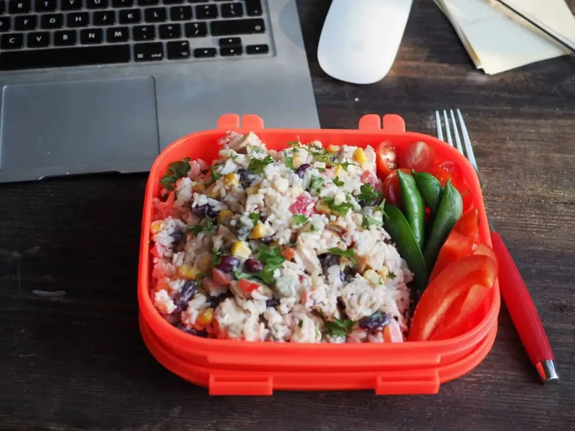 Pyszna sałatka z ryżem, kurczakiem, kukurydzą i fasolą w pomarańczowym pudełku. Obok pomidorki, groszek i papryka. Idealny lunch do pracy.
