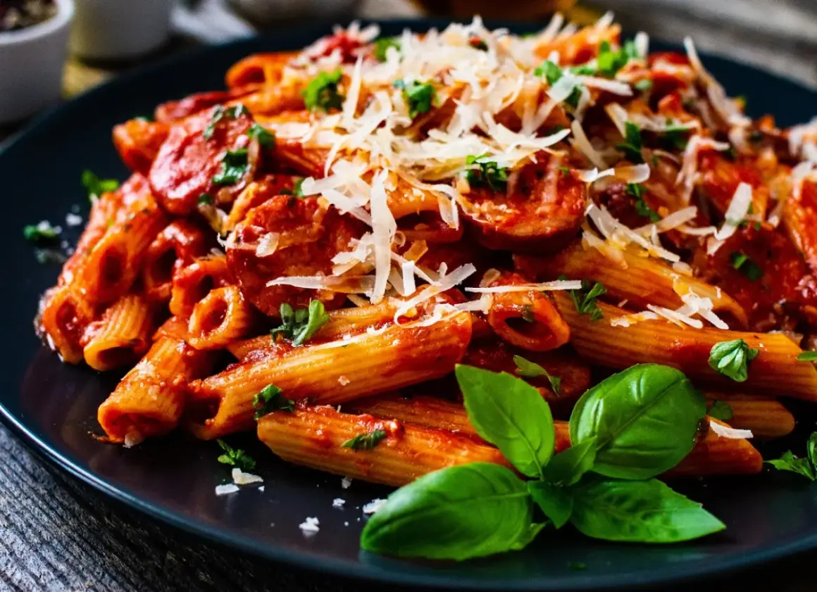 Penne z krewetkami w sosie pomidorowym, posypane parmezanem i udekorowane bazylią.