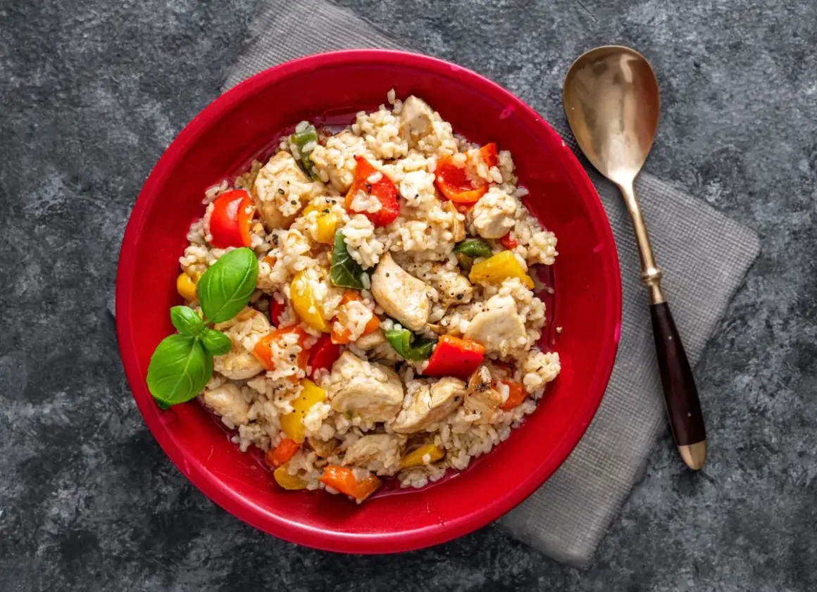 Pyszne risotto z kurczakiem, kolorową papryką i świeżą bazylią, podane w czerwonej misce.