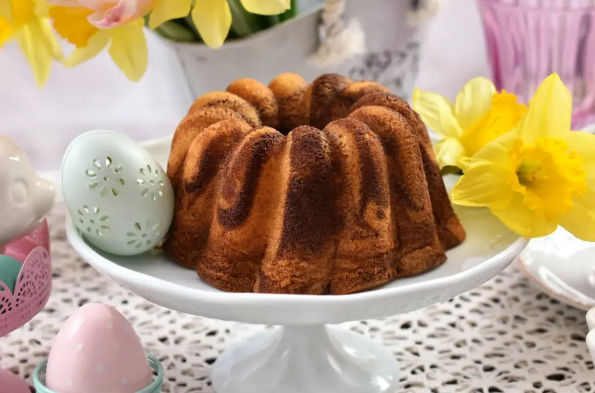 Wilgotna babka wielkanocna dwukolorowa, ozdobiona wielkanocnymi pisankami i żółtymi żonkilami, zapowiada wiosenne święta.