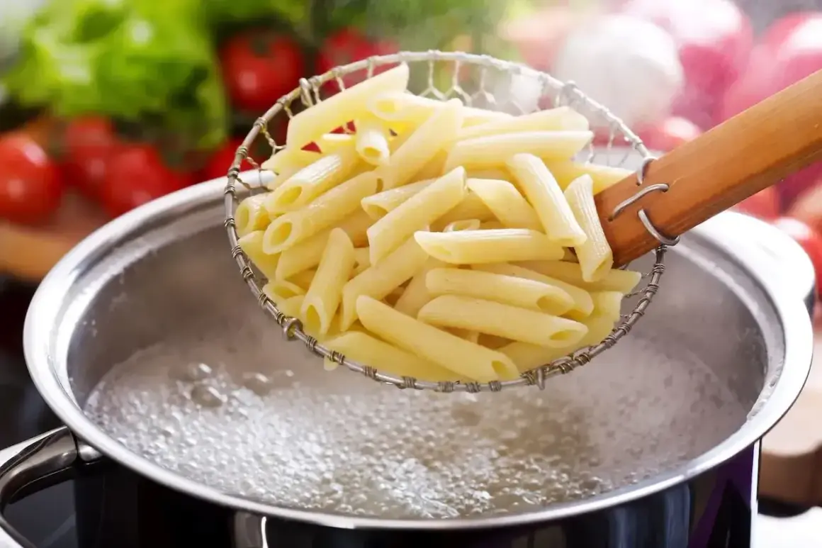 Penne makaron w cedzaku nad garnkiem z gotującą się wodą. Idealny sposób, jak ugotować makaron.