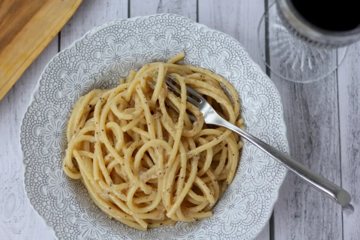 Pyszne cacio e pepe na talerzu z ozdobnym wzorem. Widok z góry na makaron spaghetti z serem i pieprzem, z widelcem w środku.
