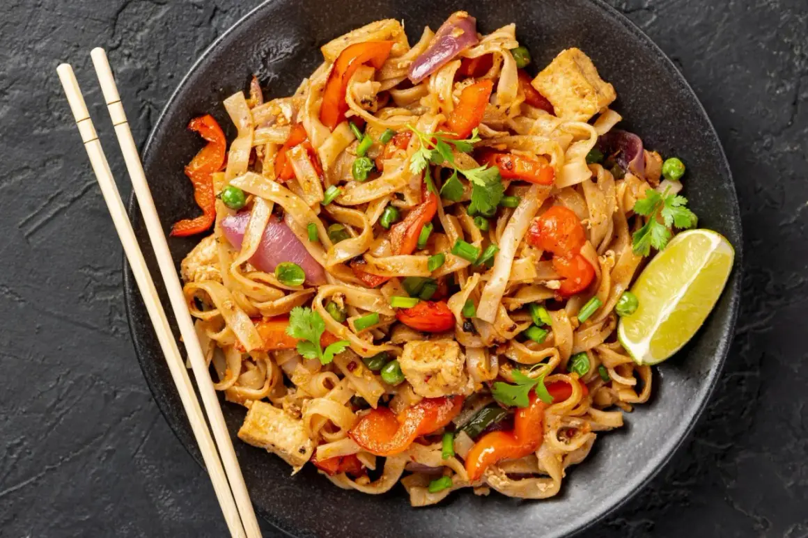 Pyszny pad thai z kurczakiem, makaronem ryżowym, warzywami i limonką.